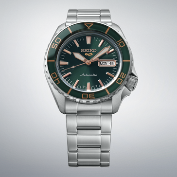 Seiko 5 Sports SKX HDB005 avec un cadran vert foncé, une lunette verte assortie, des aiguilles et des index couleur or rose, et un bracelet en acier inoxydable, présentée sur un fond gris clair.