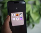 Une main tient un smartphone sur lequel s'affiche un dossier nommé « AI » contenant des applications telles que Gemini, ChatGPT et Claude.