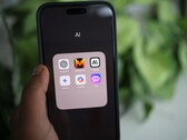 Une main tient un smartphone sur lequel s'affiche un dossier nommé « AI » contenant des applications telles que Gemini, ChatGPT et Claude.