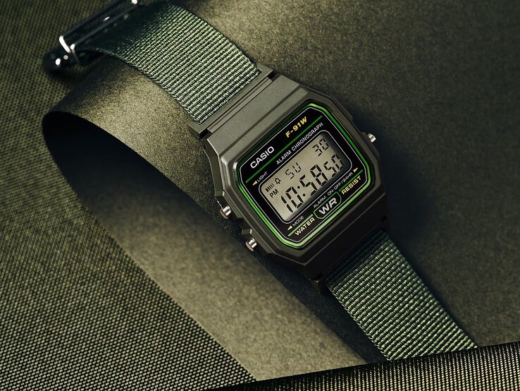 Montre numérique Casio F-91WF-3A dotée d’un boîtier noir rehaussé de touches de vert et d’un bracelet en tissu vert tressé, photographiée sur un fond texturé vert foncé.