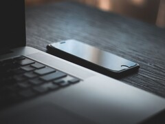 Un smartphone posé à côté d’un ordinateur portable ouvert sur un bureau sombre