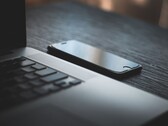 Un smartphone posé à côté d’un ordinateur portable ouvert sur un bureau sombre