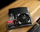 PlayStation 3 refroidie à l'eau avec une pompe SysCooling rouge et un grand ventilateur noir monté à l'intérieur du boîtier, placé sur un bureau en bois (Source de l'image : Zac Builds via YouTube)