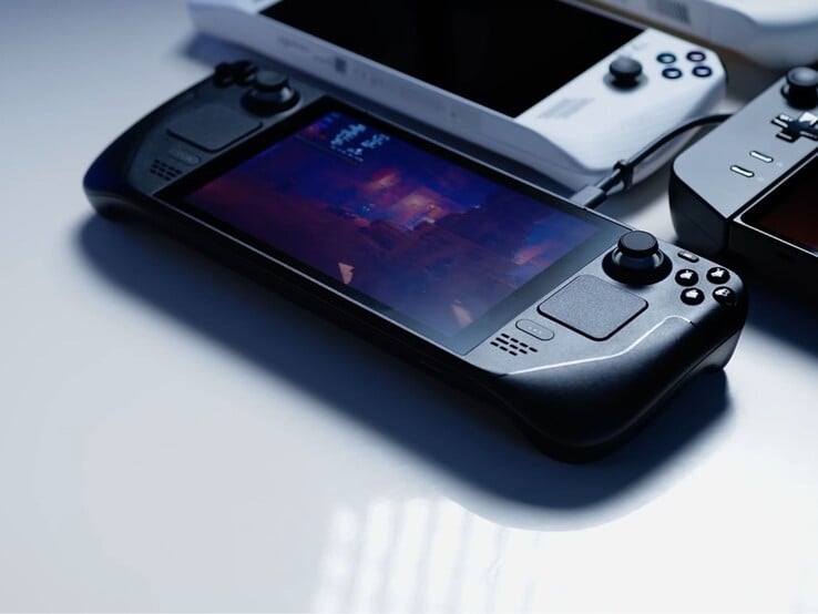 Une Steam Deck exécutant un jeu est entourée d'autres consoles de jeu portables sous un éclairage doux, avec l'étiquette à l'écran "Steam Deck Max Wattage" dans le coin supérieur gauche. (Source de l'image : Notebookcheck)
