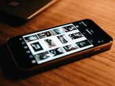 Un smartphone posé sur un bureau en bois, dont l'écran affiche une grille de photos