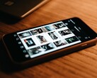 Un smartphone posé sur un bureau en bois, dont l'écran affiche une grille de photos
