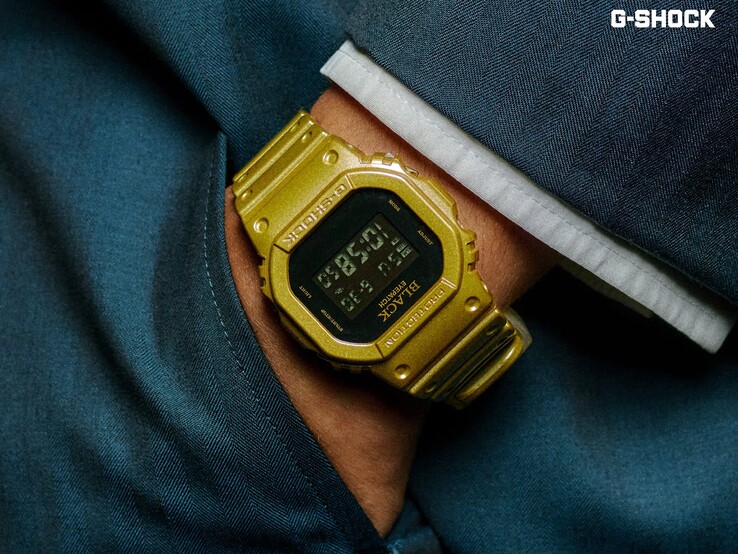 Gros plan sur une montre Casio G-Shock DW-5600BEP-9 dorée portée au poignet sur un tissu bleu foncé. La montre est dotée d’un écran numérique noir, d’un boîtier et d’un bracelet dorés, ainsi que du logo BlackEyePatch sur la lunette et le cadran.