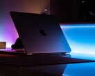 Un MacBook à demi-ouvert dans une pièce sombre, la lumière s'échappant par l'interstice et se répandant sur le bureau