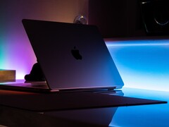 Un MacBook à demi-ouvert dans une pièce sombre, la lumière s'échappant par l'interstice et se répandant sur le bureau