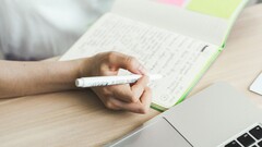 Une personne prend des notes dans un cahier à côté d'un ordinateur portable ouvert