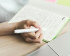 Une personne prend des notes dans un cahier à côté d'un ordinateur portable ouvert