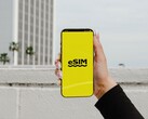 Une main tenant un smartphone sur lequel apparaît en gros le mot « eSIM » sur un écran jaune.