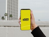 Une main tenant un smartphone sur lequel apparaît en gros le mot « eSIM » sur un écran jaune.