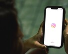 Femme tenant un smartphone à deux mains, l'écran affiche la page d'accueil d'Instagram