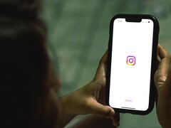 Femme tenant un smartphone à deux mains, l'écran affiche la page d'accueil d'Instagram