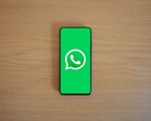 Un smartphone posé sur un bureau en bois, affichant l'écran d'accueil vert de WhatsApp avec son logo.