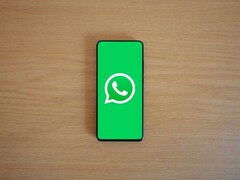 Un smartphone posé sur un bureau en bois, affichant l'écran d'accueil vert de WhatsApp avec son logo.