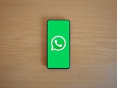 Un smartphone posé sur un bureau en bois, affichant l'écran d'accueil vert de WhatsApp avec son logo.